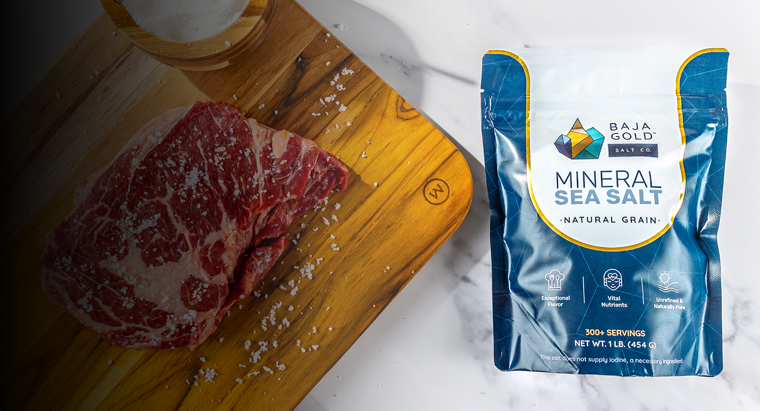 Raw meat on a cutting board with a package of Baja Gold mineral sea salt next to it.