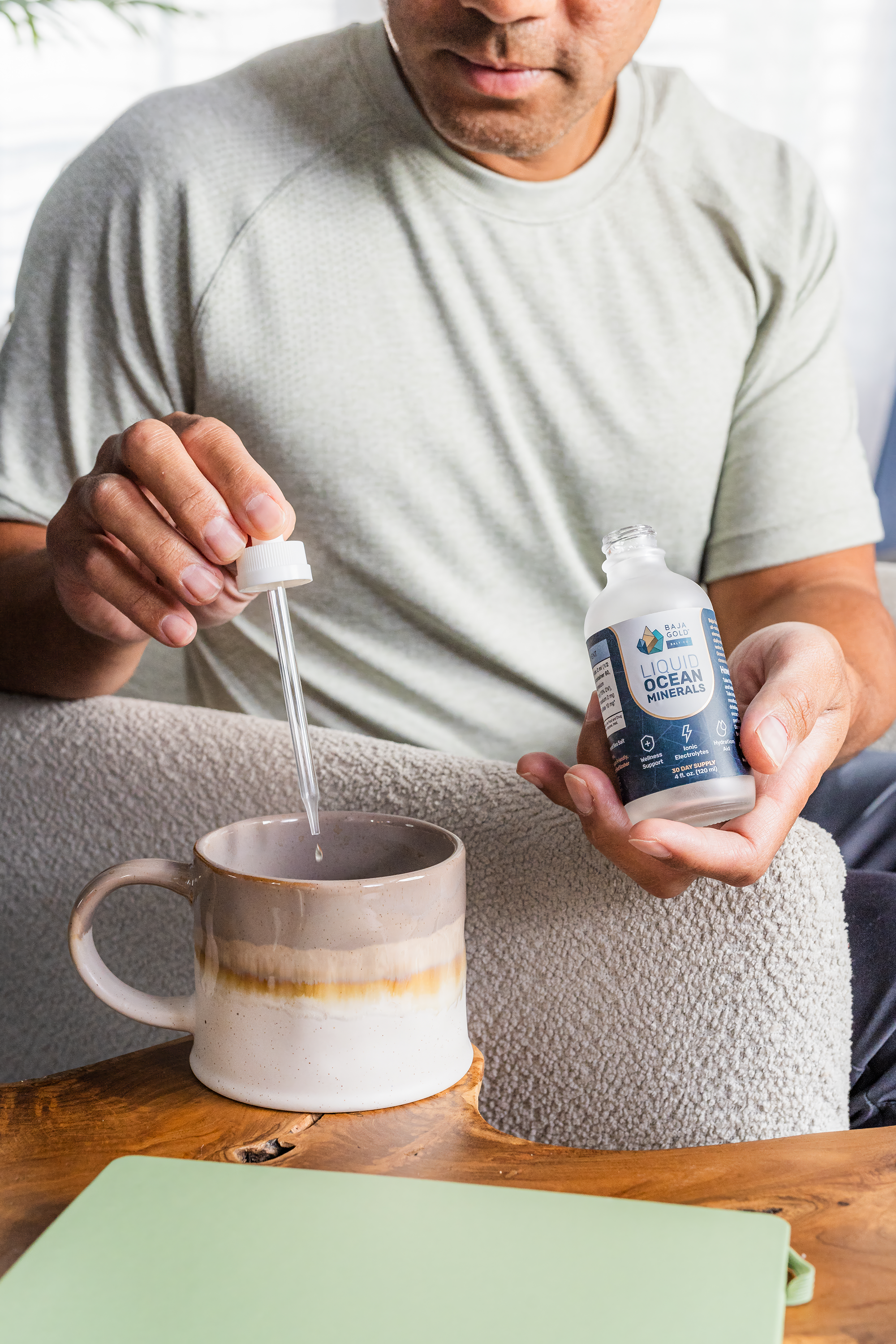 Person squeezing Baja Gold liquid ocean minerals from a bottle into a mug on a wooden table.