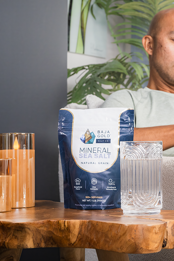 Natural grain Baja Gold mineral sea salt package on a wooden table with a glass of water and a person in the background.