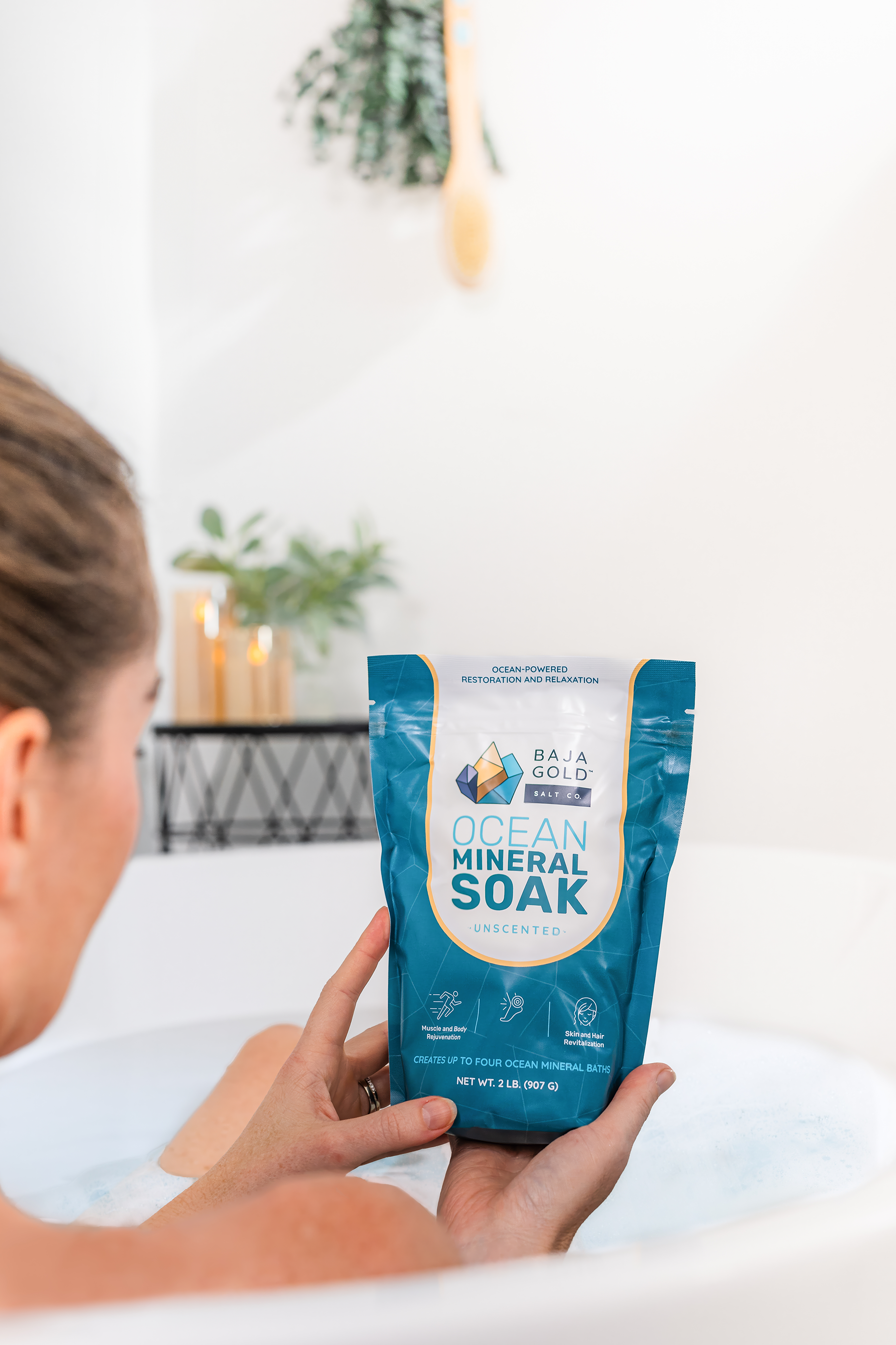 Person holding a package of unscented Baja Gold ocean mineral soak in a bathroom setting.